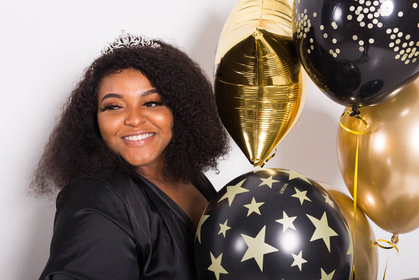 Holidays, party en fun concept - Portret van lachende jonge Afro-Amerikaanse jonge vrouw op een stijlvolle witte achtergrond met ballonnen. - Foto, afbeelding