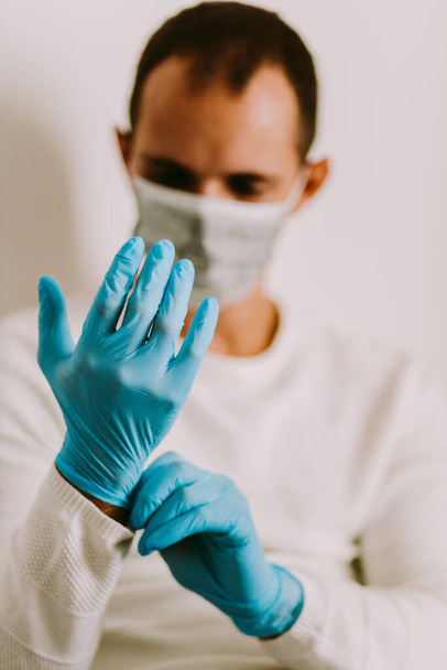Mężczyzna używający rękawic lateksowych w domu do zapobiegania wirusom. Mężczyzna noszący rękawice medyczne i maskę ochronną do zapobiegania wirusom podczas samodzielnej izolacji podczas kwarantanny. - Zdjęcie, obraz