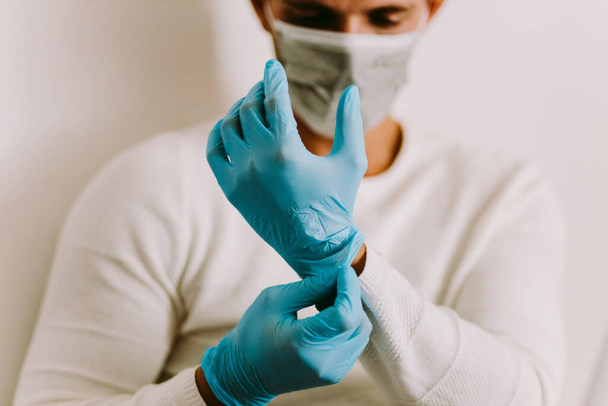 ラテックス手袋を着用し、屋内マスク男。ウイルス予防のための隔離中に自宅で働いている間、医療用手袋を使用して白人男性. - 写真・画像