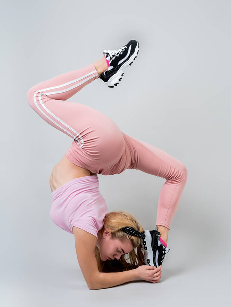Fitness, sport, training and lifestyle concept. Acrobat woman wearing pink sportswear working out in the studio isolated on gray background - Photo, Image
