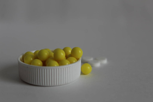 yellow vitamins are in a white lid on a white background - Zdjęcie, obraz