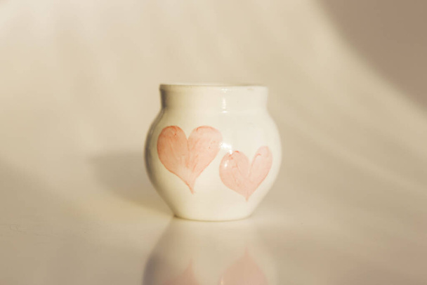kleiner weißer Topf mit zwei Herzen. Konzept Liebe. Keramikprodukt. Das Werk des Autors - Foto, Bild