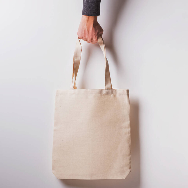 Mans hand holds blank cotton eco tote bag over the white wall - Φωτογραφία, εικόνα