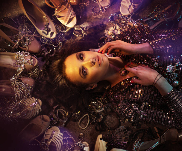 Портрет молодой, привлекательной женщины, лежащей среди множества туфель
 - Фото, изображение