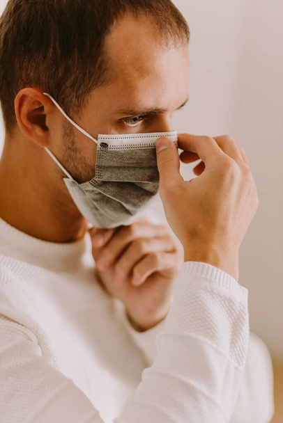 άνδρας που φοράει μάσκα προσώπου για την πρόληψη του ιού κατά τη διάρκεια της αυτοαπομόνωσης στο σπίτι. Μέτρα πρόληψης του ιού στην καραντίνα COVID-19 - Φωτογραφία, εικόνα