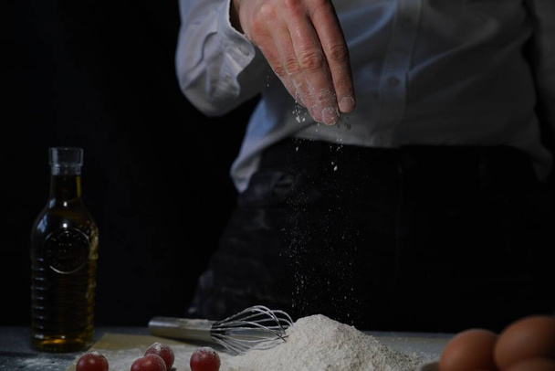 A person pouring flour from his hand onto the table to prepare food - Foto, imagen