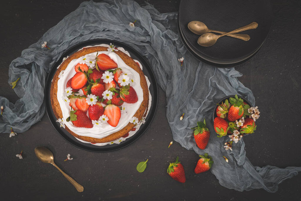 Strawberry cake, strawberry sponge cake with fresh strawberries and sour cream on a dark kitchen countertop. - 写真・画像