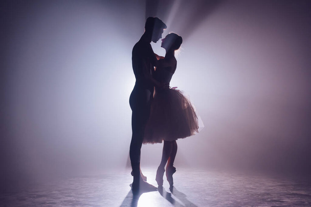 Romantic professional ballet pair looking to each other on dark stage. Young couple dancing in classic dress. Gracefulness and tenderness in every movement. - Foto, Imagem