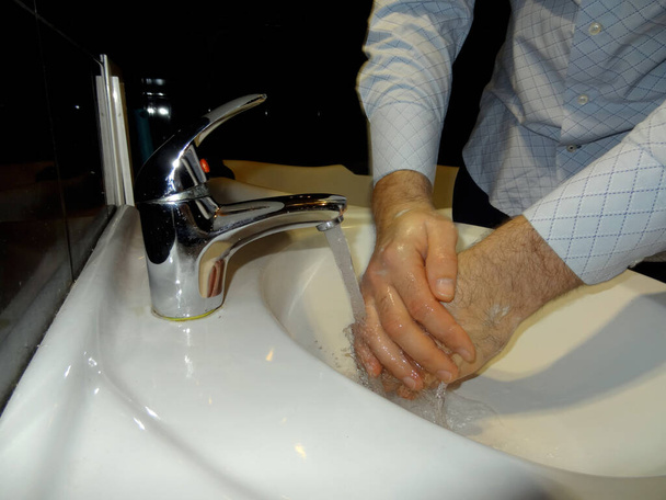 человек в рубашке дезинфицирует руки под краном в раковине
    - Фото, изображение
