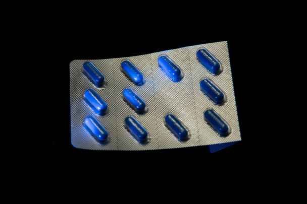 Capsule mediche ovali blu in confezione di plastica argentata su fondo nero
 - Foto, immagini