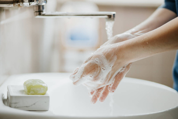 Крупним планом жінка миє руки у ванній кімнаті, щоб запобігти вірусній інфекції Ковіда-19. Рекомендоване миття з милом та водою під час пандемії коронавірусу
. - Фото, зображення