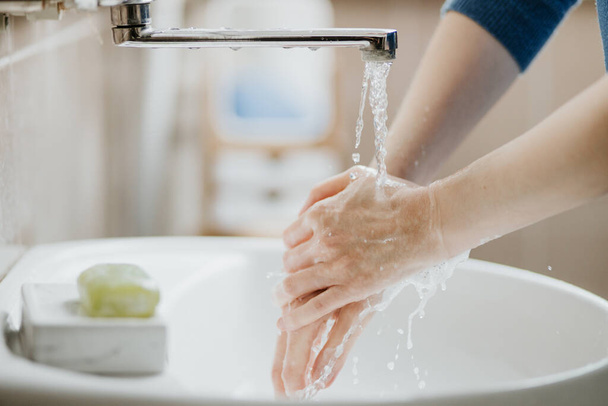 Closeup of a woman washing her hands in bathroom to prevent Covid-19 viral infection. Recommended washing with soap and running water during coronavirus pandemic. - Foto, afbeelding