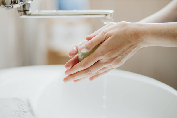 Closeup of a woman washing her hands in bathroom to prevent Covid-19 viral infection. Recommended washing with soap and running water during coronavirus pandemic. - Фото, зображення