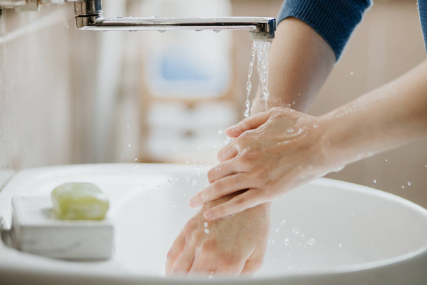 Closeup of a woman washing her hands in bathroom to prevent Covid-19 viral infection. Recommended washing with soap and running water during coronavirus pandemic. - Φωτογραφία, εικόνα