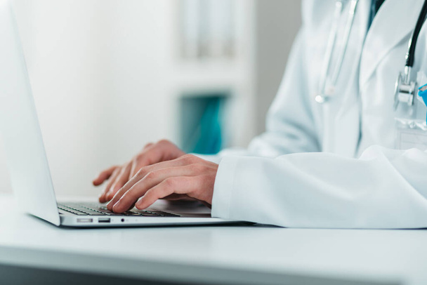 Detail mladého Doktora na práci na laptopu. Dobrovolník v nemocnici získává praktické znalosti v léčbě onemocnění - Fotografie, Obrázek