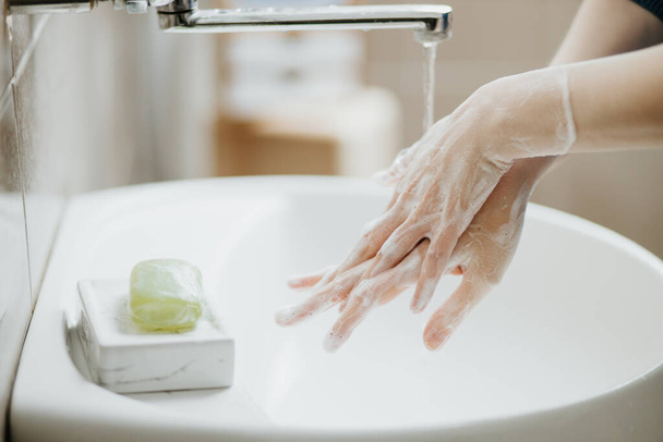 Close-up de uma mulher lavando as mãos no banheiro para evitar a infecção viral por Covid-19. Lavagem recomendada com sabão e água corrente durante a pandemia de coronavírus
. - Foto, Imagem
