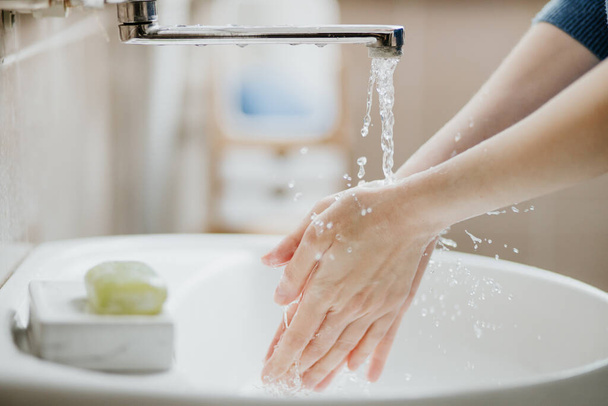 Closeup of a woman washing her hands in bathroom to prevent Covid-19 viral infection. Recommended washing with soap and running water during coronavirus pandemic. - Φωτογραφία, εικόνα