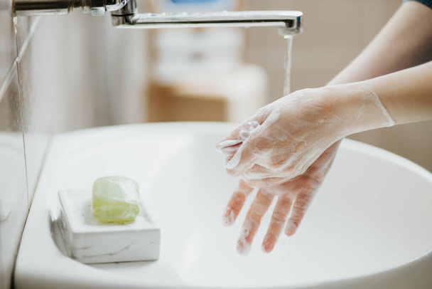 Primer plano de una mujer lavándose las manos en el baño para prevenir la infección viral por Covid-19. Lavado recomendado con jabón y agua corriente durante la pandemia de coronavirus
. - Foto, imagen