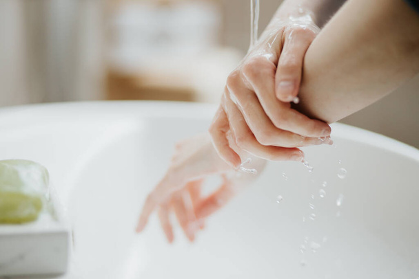 Closeup of a woman washing her hands in bathroom to prevent Covid-19 viral infection. Recommended washing with soap and running water during coronavirus pandemic. - Photo, Image