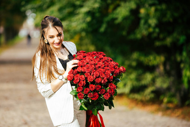 Beautiful girl in a suit with flowers in the hands of a rose on a green background. - Fotoğraf, Görsel