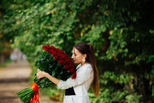 Fashionable gorgeous sexy girl in an elegant suit holding a bouquet of hundreds of red roses. Happy valentines day - Zdjęcie, obraz