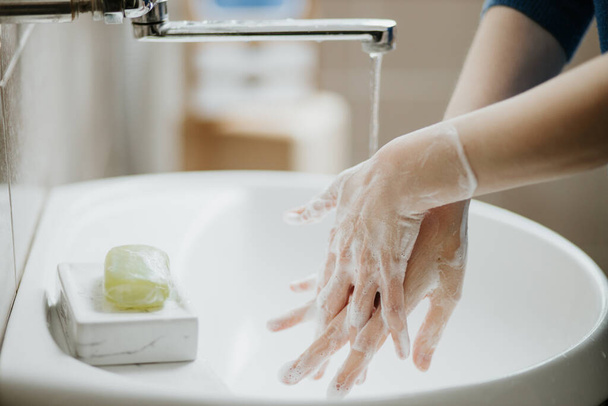 Closeup of a woman washing her hands in bathroom to prevent Covid-19 viral infection. Recommended washing with soap and running water during coronavirus pandemic. - Foto, Imagem