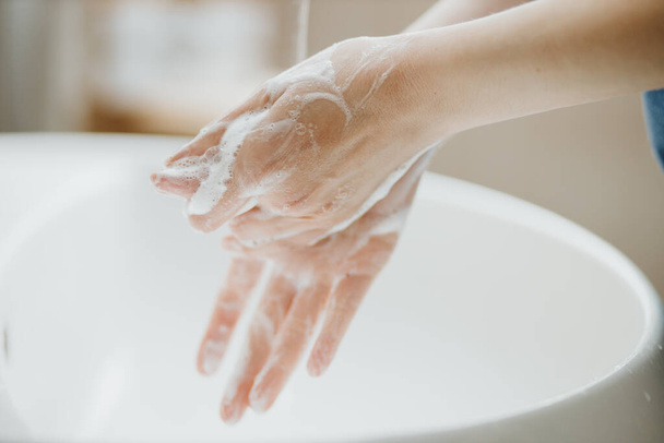 Крупный план женщины, моющей руки в ванной, чтобы предотвратить вирусную инфекцию Ковид-19. Рекомендуется мыть с мылом и проточной водой во время пандемии коронавируса
. - Фото, изображение