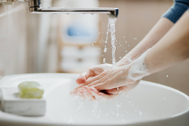 Closeup of a woman washing her hands in bathroom to prevent Covid-19 viral infection. Recommended washing with soap and running water during coronavirus pandemic. - Fotoğraf, Görsel