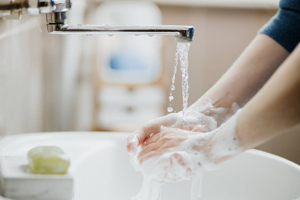 Closeup of a woman washing her hands in bathroom to prevent Covid-19 viral infection. Recommended washing with soap and running water during coronavirus pandemic. - Valokuva, kuva