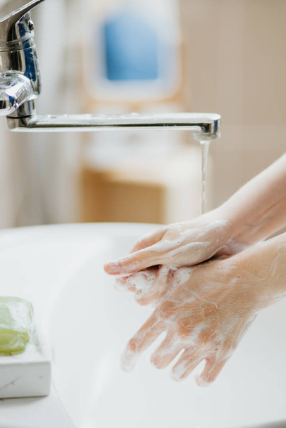 Closeup of a woman washing her hands in bathroom to prevent Covid-19 viral infection. Recommended washing with soap and running water during coronavirus pandemic. - Photo, Image
