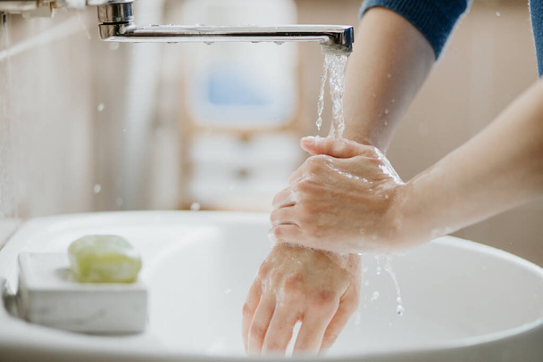 Closeup of a woman washing her hands in bathroom to prevent Covid-19 viral infection. Recommended washing with soap and running water during coronavirus pandemic. - 写真・画像