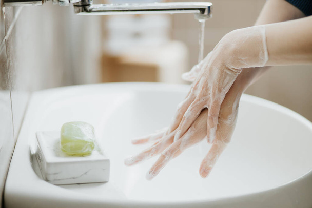 Closeup of a woman washing her hands in bathroom to prevent Covid-19 viral infection. Recommended washing with soap and running water during coronavirus pandemic. - Фото, изображение