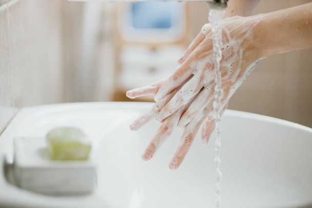 Closeup of a woman washing her hands in bathroom to prevent Covid-19 viral infection. Recommended washing with soap and running water during coronavirus pandemic. - Photo, image