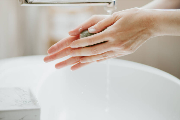 Closeup of a woman washing her hands in bathroom to prevent Covid-19 viral infection. Recommended washing with soap and running water during coronavirus pandemic. - Foto, imagen