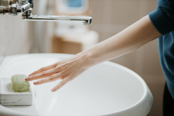 Closeup of a woman washing her hands in bathroom to prevent Covid-19 viral infection. Recommended washing with soap and running water during coronavirus pandemic. - Foto, immagini