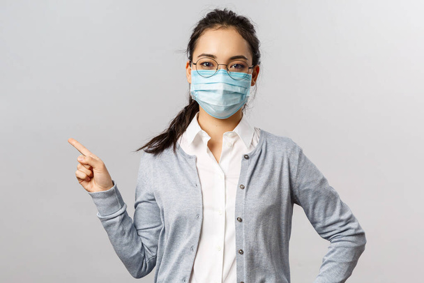 Covid19 、ウイルス、健康と医学の概念。医療用マスクの若い深刻なアジアの少女の肖像画,コロナウイルスやインフルエンザの拡散を防ぐ,左を指す,病気についての情報を示す - 写真・画像