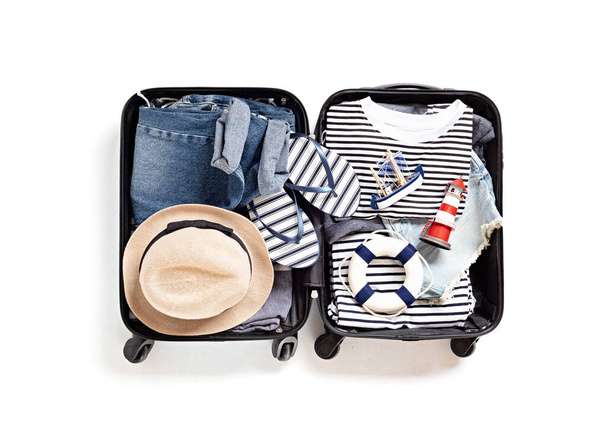 Vlak gelegd met open koffer met casual kleding voor zomervakantie over witte achtergrond. Zomervakantie, reizen, toerisme, vlucht bagage concept. Bovenaanzicht - Foto, afbeelding