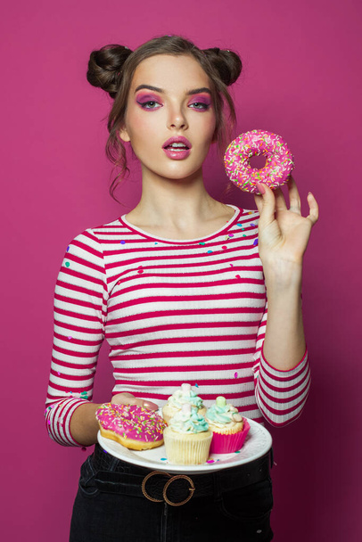 Modelo de moda bonita mulher segurando prato com sobremesa doces lanches e mostrando donut no fundo rosa vívido
 - Foto, Imagem