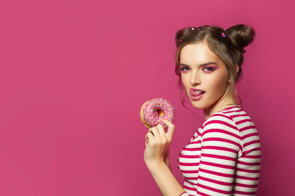 Jonge grappige vrouw met donut op kleurrijke roze achtergrond - Foto, afbeelding