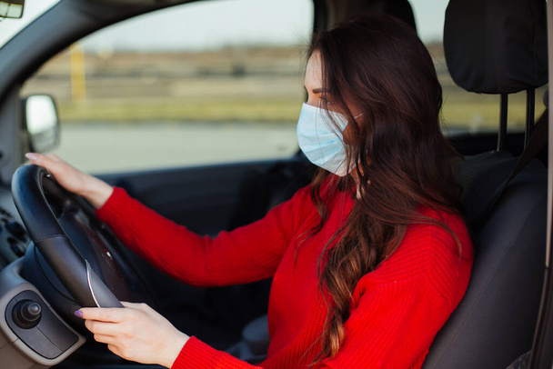 junge Frau mit Coronavirus-Maske sitzt im Auto. - Foto, Bild
