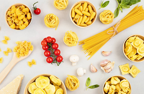 Flat lay with different types of traditional italian pasta. Penne, tagliatelle, fusilli, farfalle, spaghetti and cooking ingredients. Traditional italian cusine concept. Top view - Photo, Image
