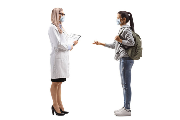 Volledig profiel shot van een vrouwelijke arts en een vrouwelijke student dragen medische maskers en praten geïsoleerd op witte achtergrond - Foto, afbeelding