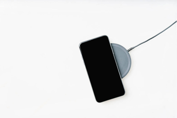 Smartphone on a wireless charger isolated over white background. Top view. Copy space. - 写真・画像