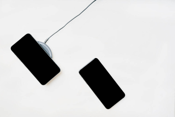 Смартфони на бездротовому зарядному пристрої ізольовані на білому тлі. Вид зверху. Копіювати простір
. - Фото, зображення