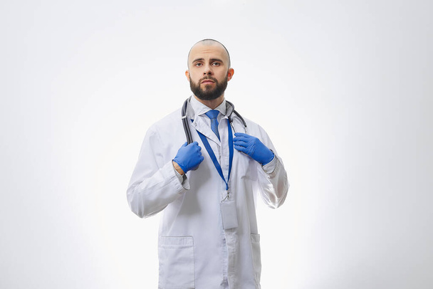 Un médico con un estetoscopio y guantes médicos desechables. Un médico calvo con barba preparándose para examinar a los pacientes
. - Foto, imagen