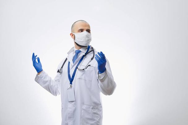 Кавказский врач в защитной маске, чтобы избежать распространения коронавируса (COVID-19) с руками в одноразовых медицинских перчатках. Лысый врач с бородой готовится к операции
. - Фото, изображение