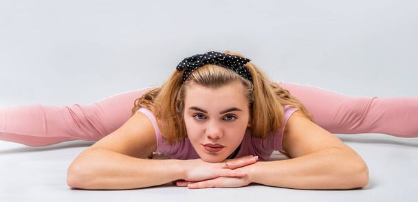 Мбаппе, спорт, тренировки и образ жизни. Молодая женщина в розовой спортивной одежде, растянувшись в позе, разделенной на ноги, в студии, изолированной на сером фоне
 - Фото, изображение