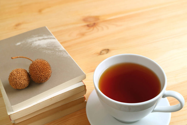 Egy csésze forró tea egy pár száraz fenyőtoboz a halom könyvet a természetes színű fa asztal - Fotó, kép