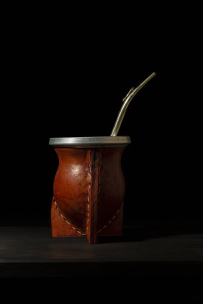 Traditional Argentine mate made in pumpkin covered in leather with a silver straw on a black background - Photo, Image