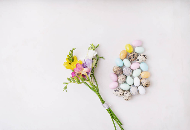 Chocolate Easter eggs glazed with pastel coloring and quail eggs over white background. Fresh colorful wildflowers. Happy Easter concept. Copy space. Top view - Foto, imagen